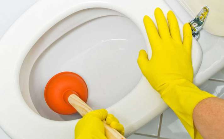 Close Up of Homeowner Trying to Unclog Toilet with Plunger