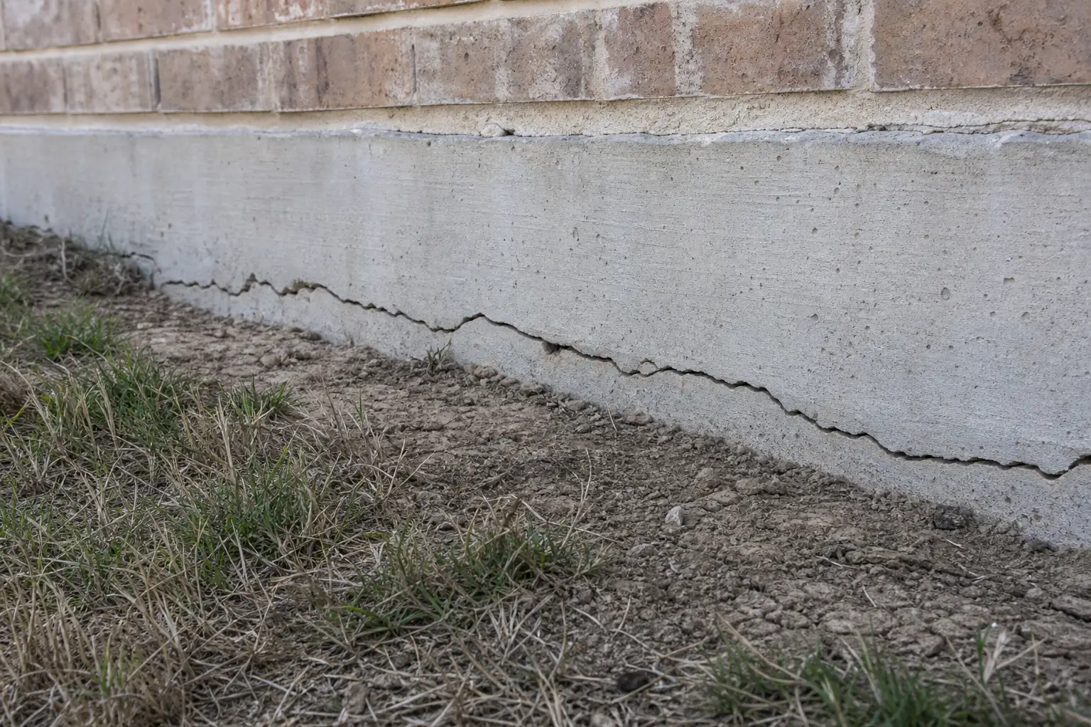 Visible crack along the base of a concrete slab foundation on a Houston home — a potential sign of soil movement from poor drainage